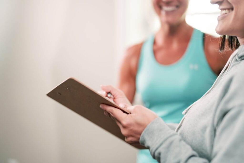 Coach en nieuwe sporter in gesprek. Geen laptop, geen afstand. Oogcontact.